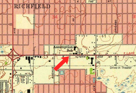 Closeup of a map with roads and buildings.  In the middle of the map is a large building labeled 'Assumption Sch' and the red arrow I added points to the intersection just south of the label for that building.