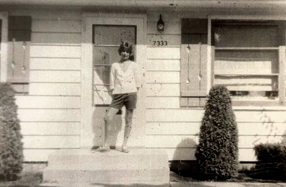 Black and white photo of a woman in front of her house.