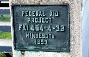 Photo showing a blue/green metal plaque on the bridge that reads 'Federal Aid Project FAI 494-4-32 Minnesota 1959.'