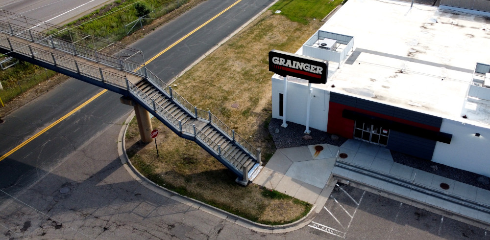 Photo of the end of the pedestrian bridge, showing that it leads to the front door of a store called Grainger.  This photo was taken from a drone.